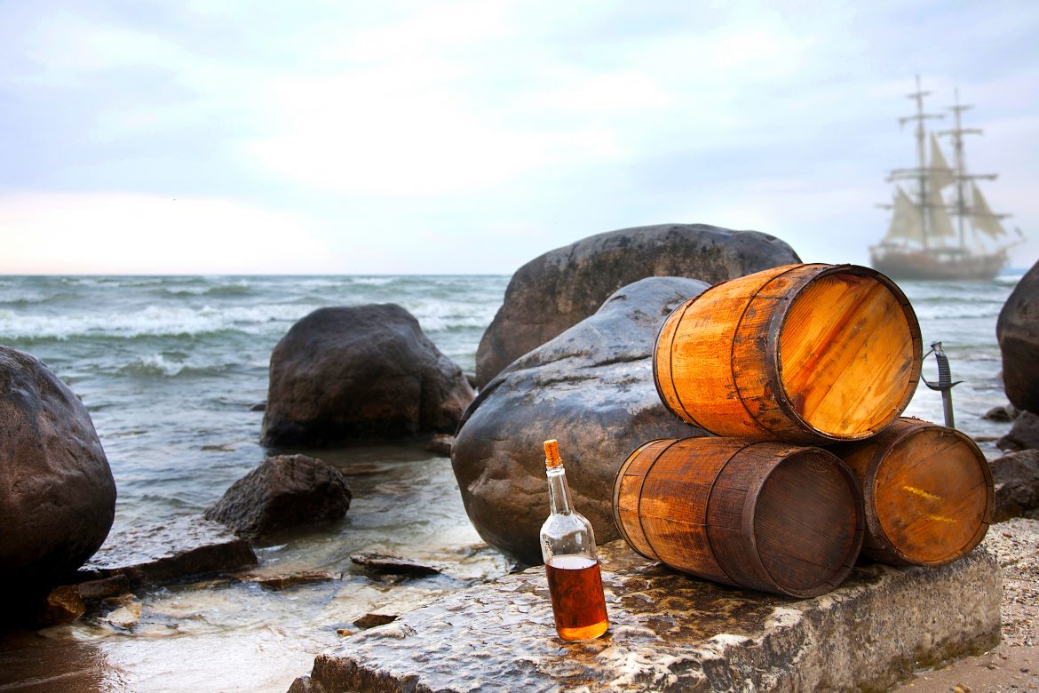 A,Pirate,Backdrop,With,Rum,And,Barrels,On,The,Beach, Rum's long history with pirates